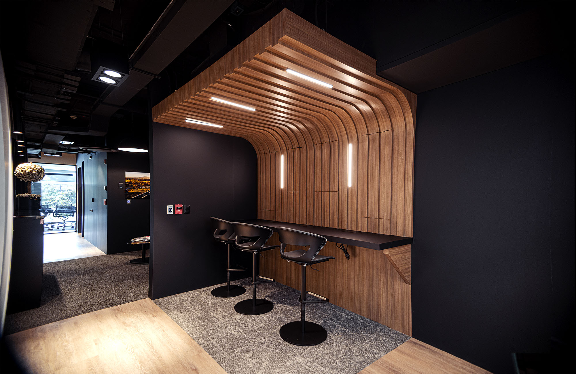 Fotografía de interiores: nicho de madera curvada con iluminación cálida y bancos altos en oficina moderna